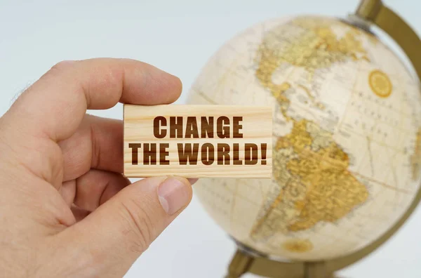 A man holds in his hand a wooden plate on which it is written - Change The World. In the background is a globe. — Stock Photo, Image