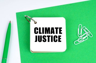 Ecology and industry concept. On a white surface lies a green sheet of paper, a pen and a notebook with the inscription - Climate justice