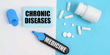 Medical concept. On the white and blue surface are pills, a marker and paper with the inscription - CHRONIC DISEASES