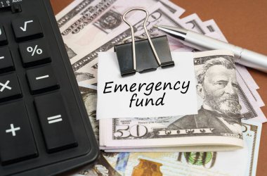 Finance and business concept. On a brown background lies a calculator and dollars on a clip with an inscription on paper - Emergency fund