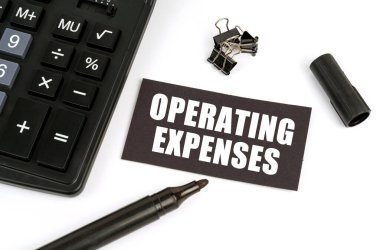 Business and finance concept. On a white table there is a calculator, a marker and a black plate with the inscription - Operating Expenses