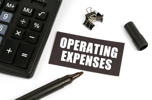 Business and finance concept. On a white table there is a calculator, a marker and a black plate with the inscription - Operating Expenses