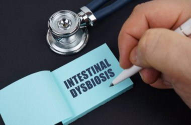 Siyah bir masada steteskop ve adamın yazdığı bir defter var. INTESTINAL DYSBIOSIS