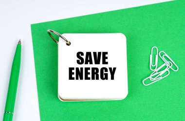Ecology and industry concept. On a white surface lies a green sheet of paper, a pen and a notebook with the inscription - save energy