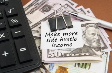 Finance and business concept. On a brown background lies a calculator and dollars on a clip with an inscription on paper - Make more side hustle income
