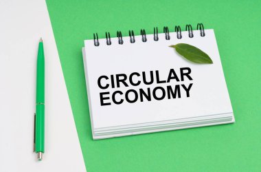 Ekolojik kavram. Beyaz-yeşil arka planda içinde yuvarlak ekonominin yazılı olduğu bir kalem ve not defteri bulunur. Defterde bir bitkinin yeşil yaprağı var..