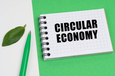 Ekolojik kavram. Beyaz-yeşil arka planda bir kalem, bir bitki yaprağı ve üzerinde yuvarlak ekonomi yazan bir not defteri bulunur.