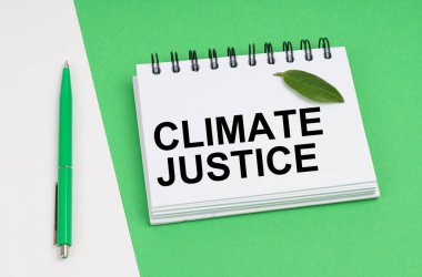 Ekolojik kavram. Beyaz-yeşil arka planda bir kalem ve üzerinde iklim adaleti yazan bir not defteri var. Defterde bir bitkinin yeşil yaprağı var..