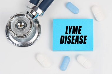 Tıp ve sağlık konsepti. Beyaz bir yüzeyde yalan hapları, steteskop ve üzerinde Lyme hastalığı yazan çıkartmalar var.