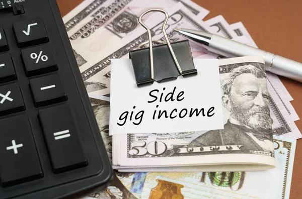 Finans ve iş konsepti. Kahverengi arka planda bir hesap makinesi ve bir şarjörde dolar ve kağıt üzerinde bir yazı bulunur - yan gelir