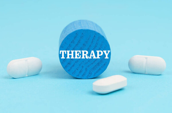 Pills lie on a blue surface, a wooden blue cylinder with the inscription - THERAPY