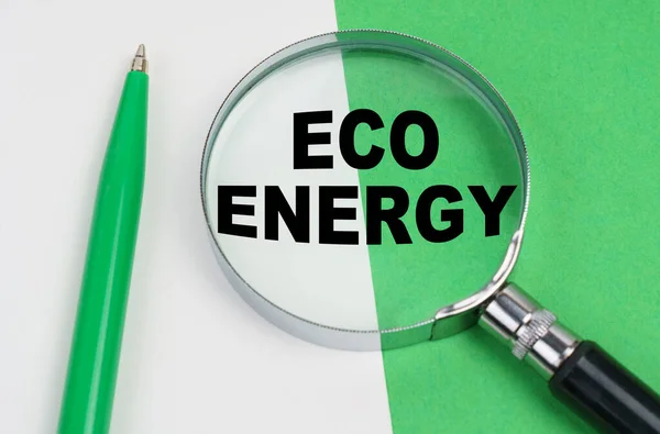 Na bílo-zeleném pozadí leží pero a lupa, uvnitř které je nápis - Eco energie — Stock fotografie
