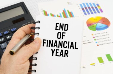 Finans ve ekonomi kavramı. Adam elinde bir kalem ve bir defter tutuyor. Finans yılının sonunda yazılmış bir defter. Arka planda finansal tablolar, çizelgeler ve bir hesap makinesi var..