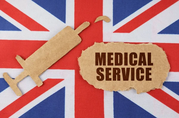 Na vlajce Velké Británie figurka injekční stříkačky a kartonu s nápisem - MEDICAL SERVICE — Stock fotografie
