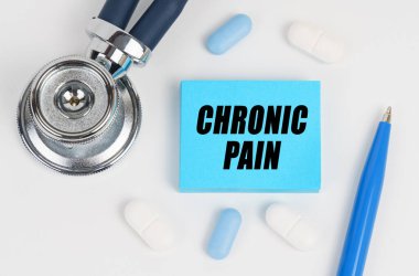 Tıp ve sağlık konsepti. Beyaz bir yüzeyde yalan hapları, bir steteskop ve üzerinde CHRONIC PaIN yazan çıkartmalar var.
