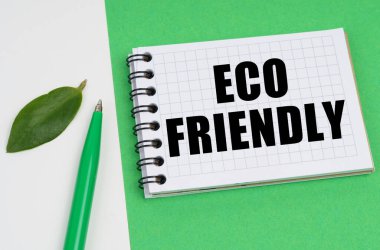 Beyaz-yeşil arka planda bir kalem, bir bitki yaprağı ve yazılı bir not defteri bulunur - ECO ARKADAŞI