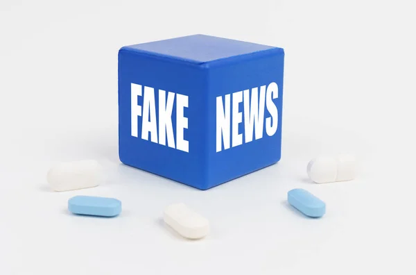 En una superficie blanca hay pastillas y un cubo azul que dice - NOTICIAS FALAS —  Fotos de Stock