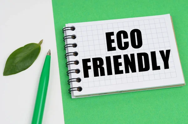 Su uno sfondo bianco-verde si trova una penna, una foglia di una pianta e un blocco note con l'iscrizione - ECO FRIENDLY — Foto Stock