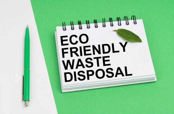 Em um fundo branco-verde encontra-se uma caneta, uma folha de uma planta e um bloco de notas com a inscrição Eco-friendly eliminação de resíduos — Fotografia de Stock