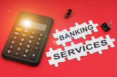 Finans ve ekonomi kavramı. Kırmızı yüzeyde bir hesap makinesi, klempler ve bulmacalar yazılı - BANING SERVICES