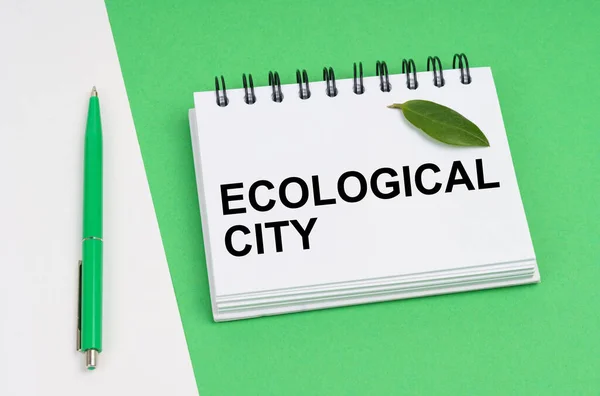 Sobre un fondo blanco-verde se encuentra una pluma, una hoja de una planta y un bloc de notas con la inscripción Ciudad Ecológica —  Fotos de Stock