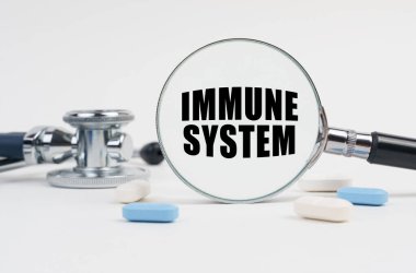 Beyaz bir yüzey yalan hapları, bir steteskop ve üzerinde IMMUNE Sistemleri yazan bir büyüteç.