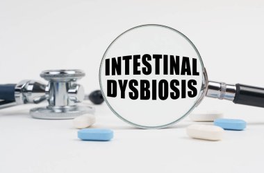 Tıp ve sağlık konsepti. Beyaz yüzey yalan hapları, bir steteskop ve üzerinde InTESTINAL DYSBIOSIS yazan bir büyüteç.