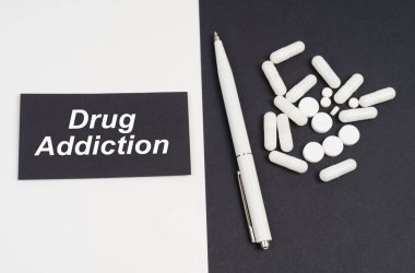 Tıbbi konsept. Beyaz ve siyah yüzeyde haplar, bir kalem ve yazılı bir tabela var.