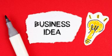 İş konsepti ve fikri. Kırmızı bir yüzey üzerinde bir işaret, bir ampul çizimi ve yırtılmış bir kağıt bulunur - BUSINESS IDEA