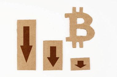 Ekonomide kriz kavramı. Beyaz bir yüzeyde, aşağı okları ve bitcoin sembolü olan bir grafik. Kartondan yapılmış sembol ve grafik