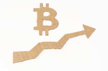Ekonomik büyüme kavramı. Beyaz bir yüzeyde, yukarı ok ve bitcoin sembollü bir grafik. Sembol, ok ve grafik kartondan yapılmıştır