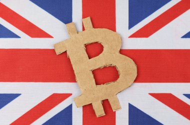 Kripto para birimi konsepti. İngiliz bayrağının kartondan kesilmiş bir bitcoin sembolü var..