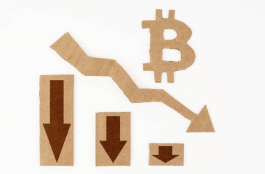 Ekonomide kriz kavramı. Beyaz bir yüzeyde, aşağı okları ve bitcoin sembolü olan bir grafik. Sembol, ok ve grafik kartondan yapılmıştır