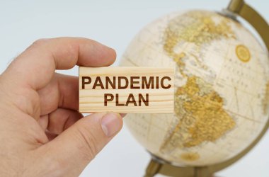 Küreselleşme kavramı. Bir adam elinde, üzerinde PANDEMIC Planı yazan ahşap bir tabak tutar. Arka planda bir küre var..