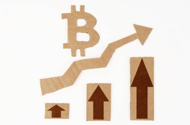 Ekonomik büyüme kavramı. Beyaz bir yüzeyde, yukarı ok ve bitcoin sembollü bir grafik. Sembol, ok ve grafik kartondan yapılmıştır