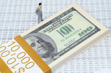 İş konsepti. Finansal raporlarda bir yığın dolar ve bir iş adamının minyatür bir figürü yatıyor.
