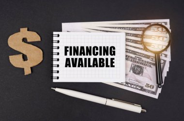 İş ve finans kavramı. Siyah bir yüzey üzerinde dolar, bir sembol, bir büyüteç, bir kalem ve bir not defteri bulunur.