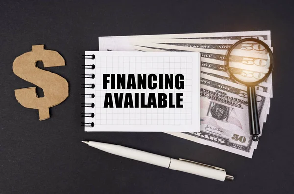 İş ve finans kavramı. Siyah bir yüzey üzerinde dolar, bir sembol, bir büyüteç, bir kalem ve bir not defteri bulunur.