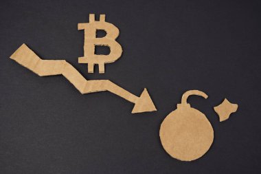 Ekonomik kriz kavramı. Siyah bir yüzeyde, aşağı ok, bitcoin sembolü ve bomba olan bir grafik. Sembol ve ok kartondan yapılmıştır.