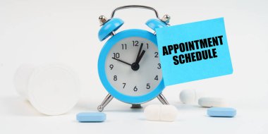 Tıbbi konsept. Beyaz bir yüzey üzerinde haplar ve alarm saati var, üzerinde bir etiket var - APPOINTMENT ScheDULE