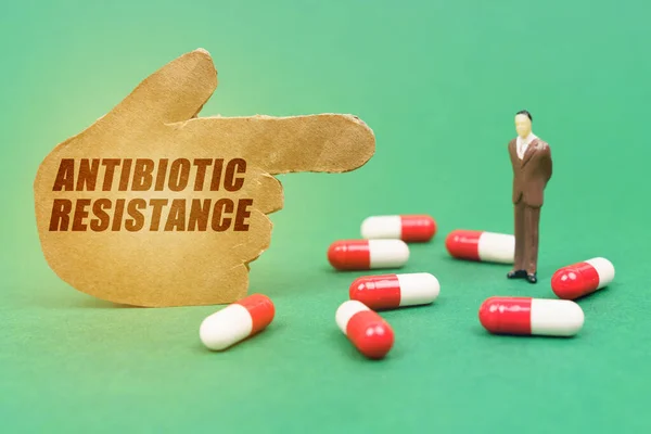Tıp ve sağlık konsepti. Yeşil arka planda kapsüllerdeki haplar, bir adamın minyatür figürü ve üzerinde AnTIBIOTIC RESİSTANS yazan bir el var.