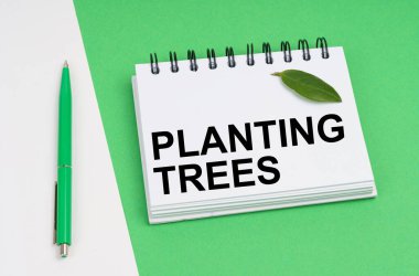 Ekolojik kavram. Beyaz-yeşil arka planda bir kalem ve üzerinde ağaç dikme yazılı bir not defteri bulunur. Defterde bir bitkinin yeşil yaprağı var..