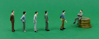 Ekonomik konsept. Minyatürler. Patron sikkelerin üzerine oturur, insanların figürleri yakınlarda durur. Pankart
