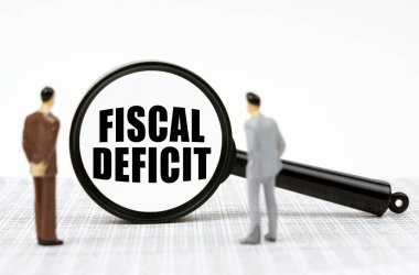 İş ve finans kavramı. Finansal raporlarda iş adamlarının minyatür figürleri ve üzerinde FISCAL DEFICIT yazan bir büyüteç var.