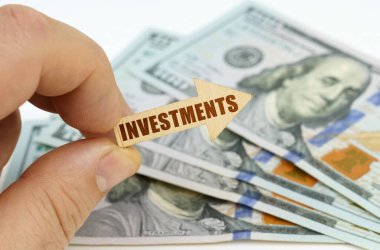 İş ve finans kavramı. Bir adamın elinde, üzerinde yazı olan bir ok vardır. Yatırımlar, arka planda dolar vardır..