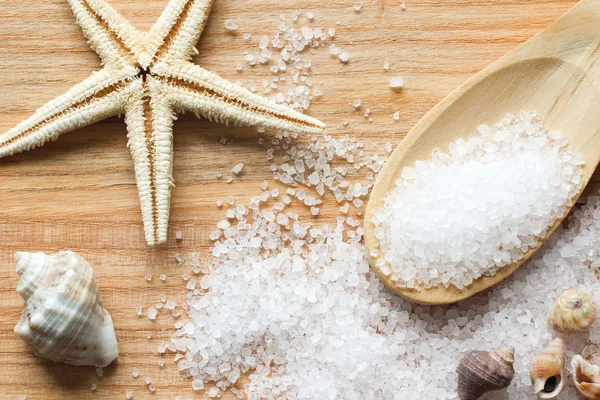 Cristales de sal marina en cuchara de madera con conchas marinas y estrellas de mar sobre fondo de madera —  Fotos de Stock