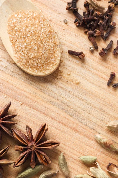 Wooden background with brown sugar crystals, star anise, cardamom and cloves for cooking — Stock Photo, Image