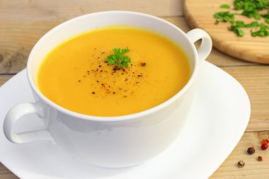 Beyaz kase taze yeşil bitkiler ile ahşap tabloda vejetaryen balkabağı çorbası