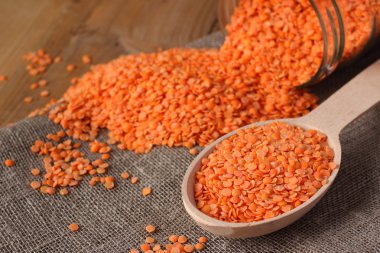 Refined red lentils in wooden spoon and glass jar on linen sackcloth clipart