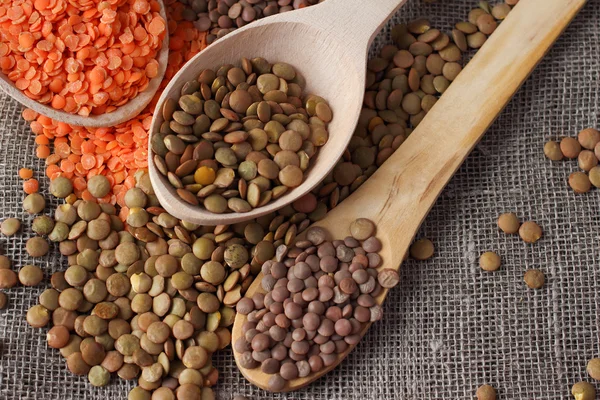 Green and red lentils in wooden spoons on sackcloth — Stock Photo, Image